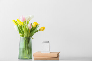 Flip paper calendar, notebooks and vase with flowers on table