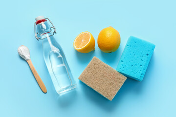 Bottle of vinegar, baking soda, sponges and lemons on color background