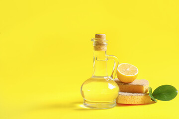 Jug of vinegar, sponges and lemon on yellow background