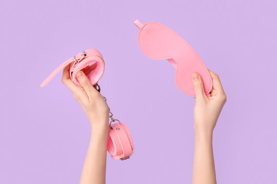 Woman with pink handcuffs and mask from sex shop on lilac background