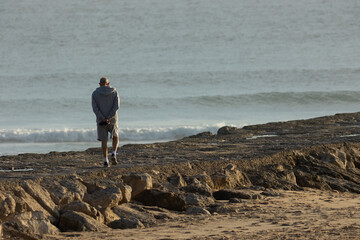 A lonely elderly man walks on a rocky ledge by the sea