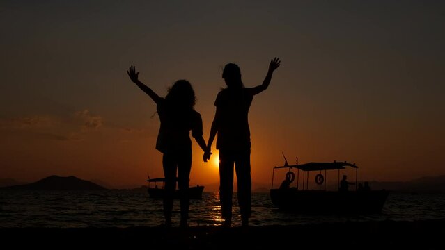 Happy children at sunset. The silhouette of little girls joyfully raised their hands, enjoying the sea sunset.