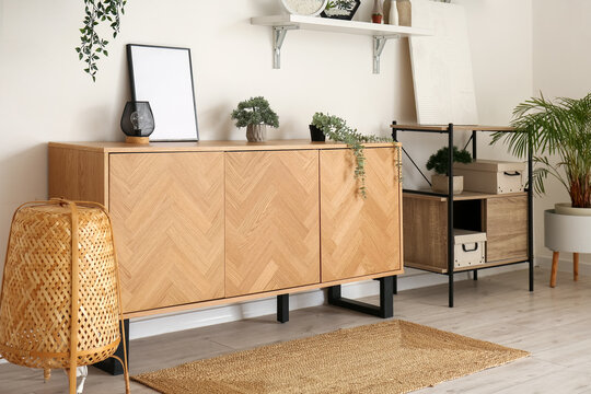 Stylish wooden cabinet with houseplants and blank frame in interior of room