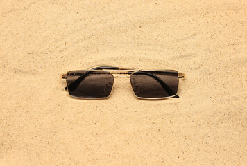 Stylish sunglasses on sand, top view
