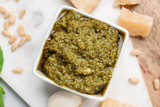 Board with bowl of delicious pesto sauce and ingredients, closeup