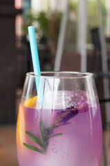close up of a colorful purple beverage with a flower and orange slice garnish with an aqua straw and soft focus restaurant background