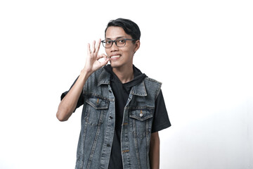 Asian man wearing sleeveless blue jean jacket giving ok or thumbs up sign that he agrees. Isolated white background