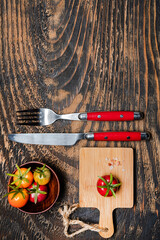 one ripe cherry tomatoes on cutting board.Fork and knife on dark wooden table. view from above.