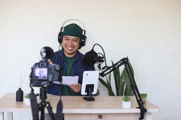 Smiling young Asian male vlogger influencer in headphones recording at podcast studio. Man blogger...
