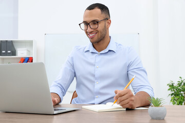 Happy young intern working with laptop at table in modern office