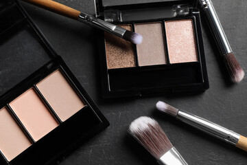 Beautiful eye shadow palettes and brushes on dark grey textured table, flat lay