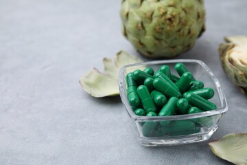 Bowl with pills and fresh artichokes on grey table, closeup. Space for text