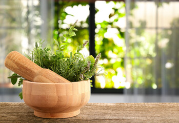 Mortar and different herbs on wooden table in room, space for text