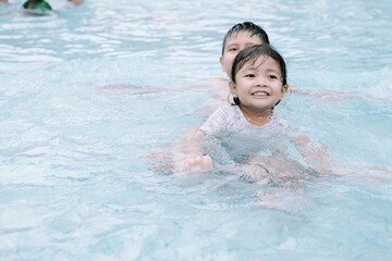 Two Southeast Asian children playing in the water at a swimming pool. Soft focus or unfocused.