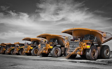 Massive yellow excavation trucks lined up. Used for transporting mine ore. Industrial transportation. Spot color yellow. All logos removed.
