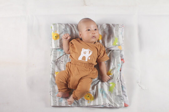 Portrait of a two month old boy looking at camera cutely and smiling as he sleeps in brown clothes in newborn baby photo shoot
