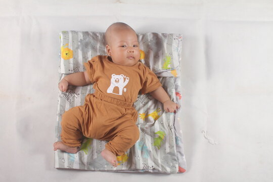 Portrait of a two month old boy looking at camera cutely and smiling as he sleeps in brown clothes in newborn baby photo shoot
