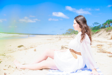 Fototapeta na wymiar 砂浜に座る白い服を着た白人少女の横顔