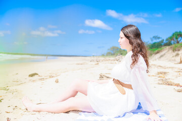Fototapeta na wymiar 砂浜に座る白い服を着た白人少女の横顔