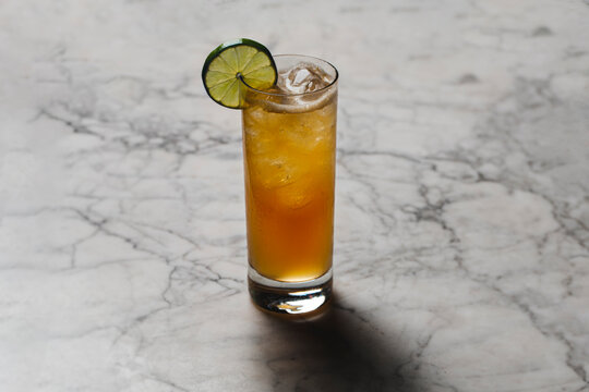 Classic highball collins drink on fancy marble top in cocktail lounge with lime wheel garnish.