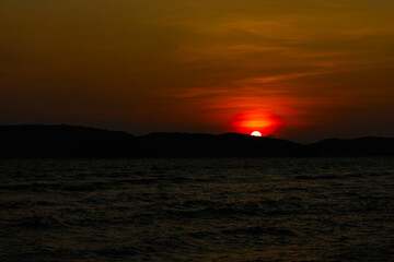 Beautiful blazing sunset landscape at dark sea and mountain with orange sky
