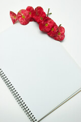 White blank notebook and a red Crown of Thorns flower (Euphorbia milii) background. Vertical