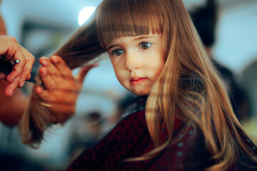 Naklejka premium Adorable Toddler Girl Getting her Hair Cute in a Professional Salon. Little preschool child having a haircut in a beauty studio 