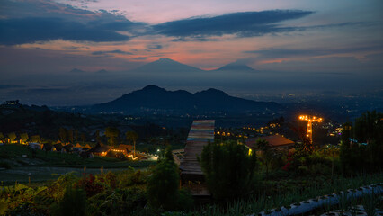 Obraz premium Beautiful reddish orange sunrise sky with mountain range and plantation on the foreground - Mangli Sky View Tourist attraction on slope Sumbing Mountain, Indonesia