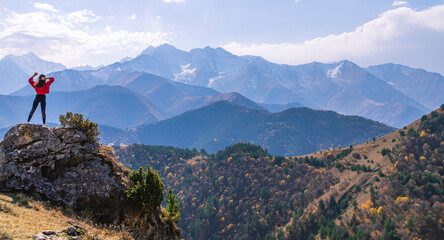 A slender girl with long dark hair looks into the distance at the snow-capped mountain peaks....