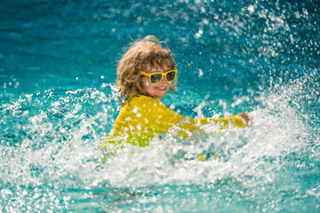 Fototapeta na wymiar Excited child swimming. Little kid playing in blue water of swimming pool on a tropical resort at the sea. Cute boy swimming in pool water. Child splashing and having fun in swim pool.
