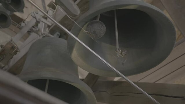 Giant church bell moving while carillon player plays a song in low angle LOG