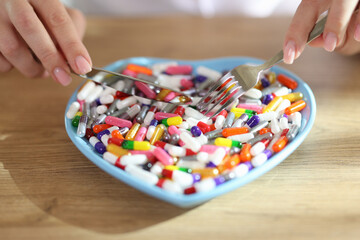 Female hands holding fork and knife and pills in heart-shaped bowl