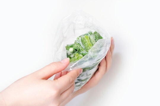 Female hands hold package of frozen string beans on white background.