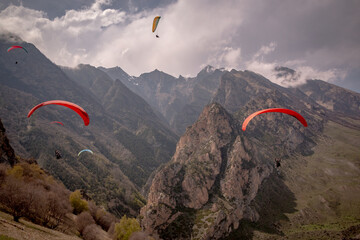 A paraglider flies among the rocky mountains and clouds. A sunny spring day.