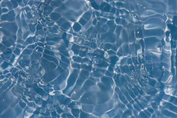 Blue water with ripples on the surface. Defocus blurred transparent blue colored clear calm water surface texture with splashes and bubbles. Water waves with shining pattern texture background.