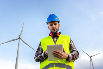 Male maintenance worker wearing helmet and vest checking data on digital tablet.