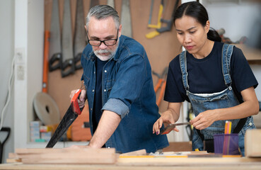Happy multicultural couple working together at wood carpenter workshop. Portrait, Asian wife standing with her bearded craftsman renovation DIY furniture. Diversity ethnic family in artisan woodwork