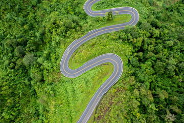 Top view of countryside road passing through the green forrest and mountain