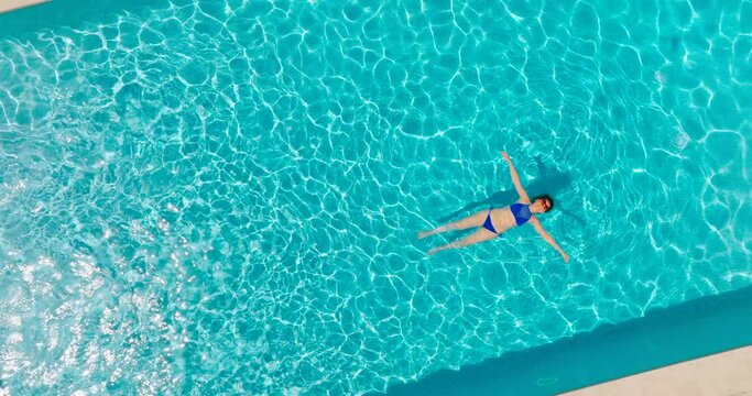 Top down view of a woman in blue swimsuit lying on her back in the pool.