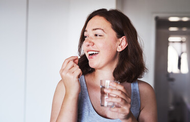 Healthcare, medication and woman drinking a pill with a glass water for wellness at her home. Medicine, medical and happy female person taking a vitamin, supplement or tablet with liquid in apartment