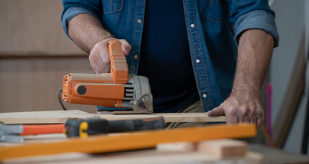 Carpenter working with wood using hand tool, equipment at workshop. American handyman use electric planer on wooden plank in home craft carpentry. Joiner woodworking and furniture making industry.