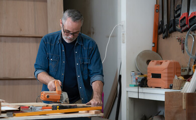 Carpenter working with wood using hand tool, equipment at workshop. American handyman use electric planer on wooden plank in home craft carpentry. Joiner woodworking and furniture making industry.