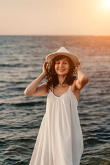 woman sea sunset. A woman in a dress, hat and with a straw bag is standing on the beach enjoying the sea. Happy summer holidays.