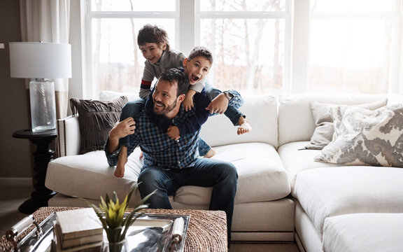 Father, Boy Children And Playing In Living Room, Fun And Carefree With Love, Energy And Happy At Family Home. Man Play With Kids On Sofa, Crazy And Playful With Piggyback And Excited With Laughter