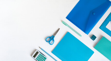 Blue green stationery in the corner and copy space. Accessories for writing and counting on a white table, a notebook, a ruler, scissors, a pencil, a pen.