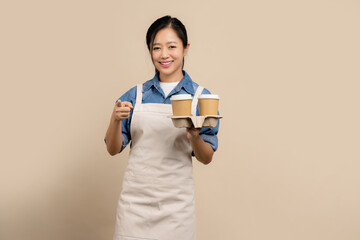 Small business owner of young asian woman in apron with hand holding cup of coffee isolated on...
