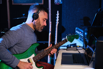Musician man playing electric guitar with headphones at home recording studio.