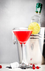 Cosmopolitan alcoholic cocktail drink with vodka, liqueur, cranberry juice, lime and ice. Gray table background, bar tools, copy space