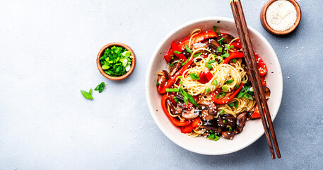 Vegan stir fry noodles with vegetables, paprika, mushrooms, chives and sesame seeds in bowl. Asian cuisine. Gray table background, top view