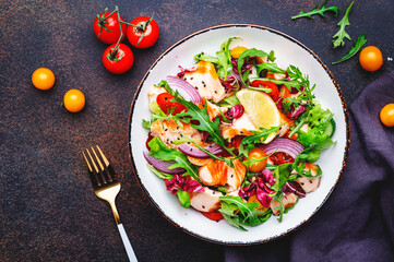 Gourmet salad with grilled salmon with tomatoes, cucumber, arugula, radicchio, red onion and lettuce with lemon oil dressing. Healthy lunch. Brown stone table background, top view